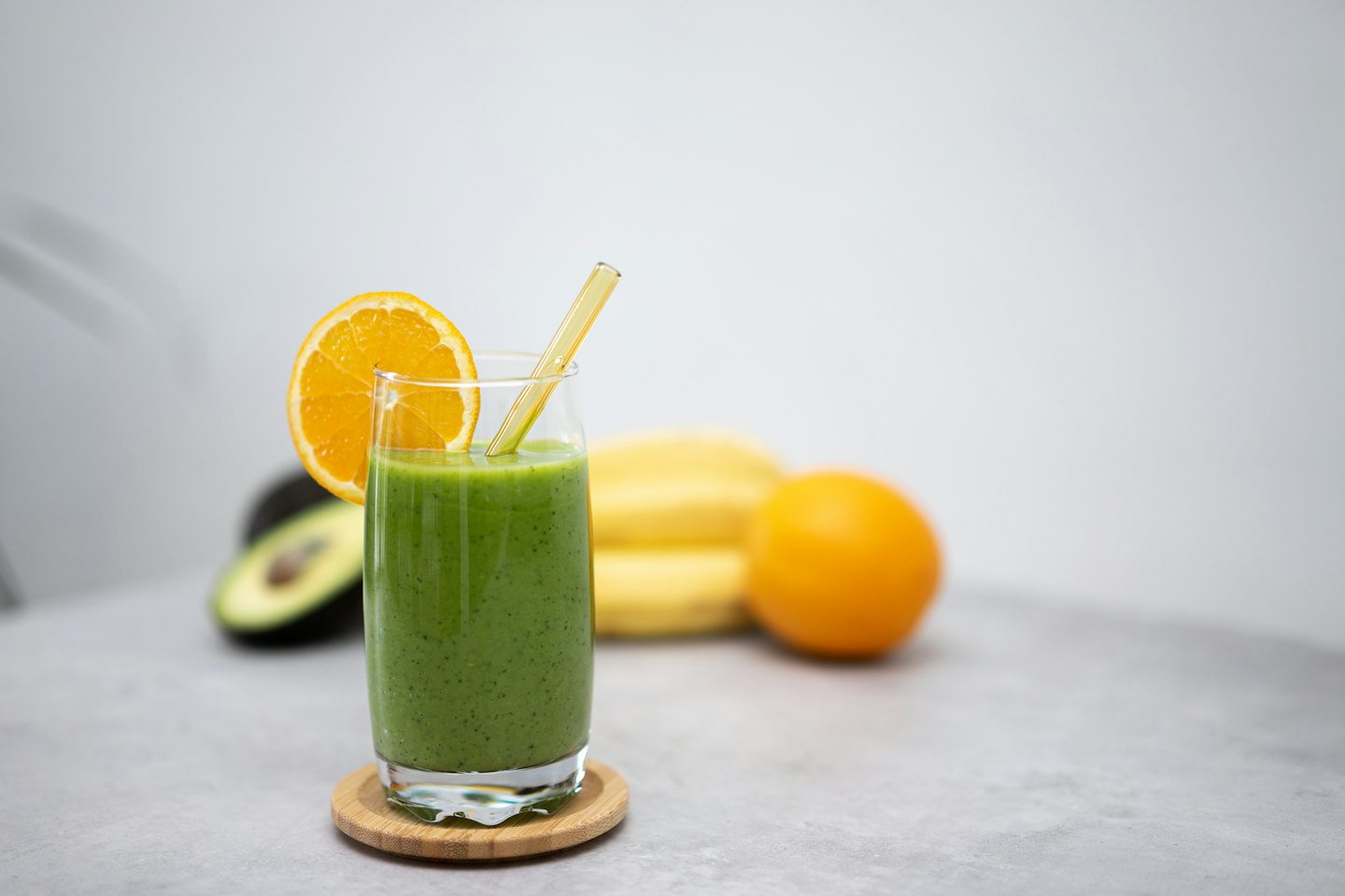 Zelené smoothie s plátkom pomaranča a slamkou na drevenom tácke.